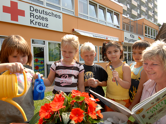 Abbildung: DRK - KiTa 'Regenbogen' im Stadtteil Lohbrügge in Hamburg: Erzieherin und Kinder beim Pflegen der Blumen im Garten