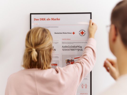 Abbildung zeigt Frau vor einem Poster der DRK Gestaltungselemente