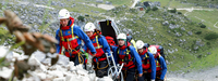 Übung der Bergwacht bei Garmisch-Partenkirchen. Team läuft einen Hang aufwärts, eine Gebirgstrage wird mitgeführt.