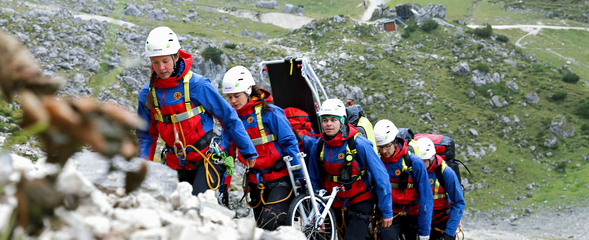 Übung der Bergwacht bei Garmisch-Partenkirchen. Team läuft einen Hang aufwärts, eine Gebirgstrage wird mitgeführt.