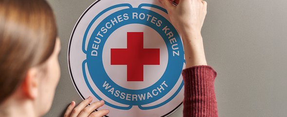 Person klebt Wasserwacht Sticker an eine Wand