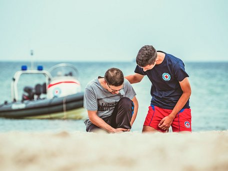 Wasserwacht an der Ostsee in Mecklenburg-Vorpommern: Verletzter mit umgeknicktem Fuß am Strand und Helfer der Wasserwacht